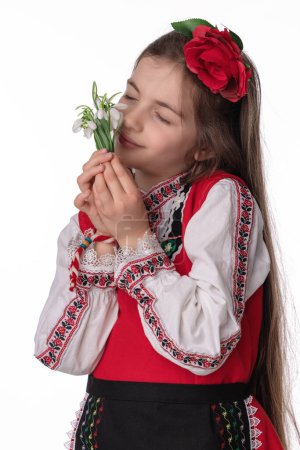 Foto de Chica búlgara en trajes folclóricos tradicionales con flores de gota de nieve y artesanía pulsera de lana martenitsa símbolo de Baba Marta, vacaciones de primavera y Pascua, martisor - Imagen libre de derechos