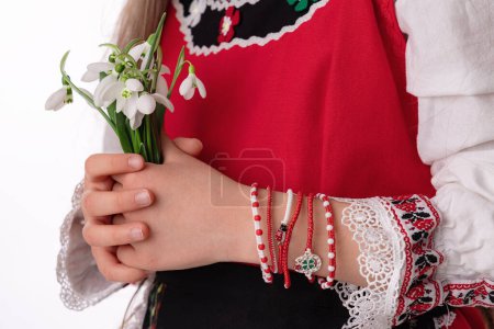 Photo for Bulgarian girl in traditional folklore costumes with snowdrop flowers and handcraft wool bracelet martenitsa symbol of Baba Marta, spring and Easter holiday,martisor - Royalty Free Image