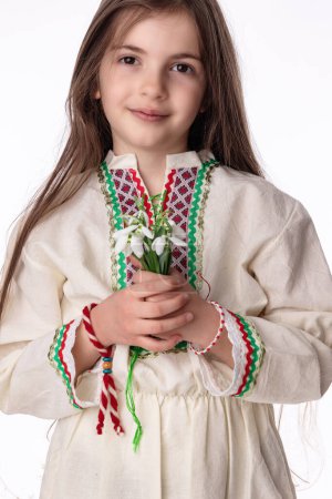 Bulgarian girl in traditional folklore costumes with snowdrop flowers and handcraft wool bracelet martenitsa symbol of Baba Marta, spring and Easter holiday,martisor