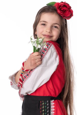 Photo for Bulgarian girl in traditional folklore costume with bouquet spring snowdrop flowers and wool bracelet martenitsa symbol of March holiday Baba Marta - Royalty Free Image