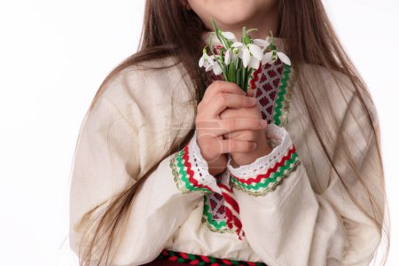 Photo for Bulgarian girl in traditional folklore costume with bouquet spring snowdrop flowers and wool bracelet martenitsa symbol of March holiday Baba Marta - Royalty Free Image
