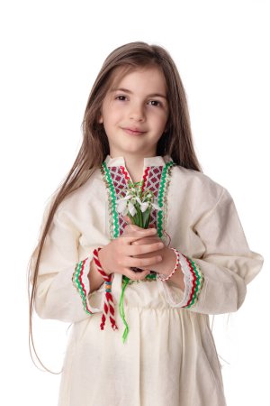 Foto de Chica búlgara en trajes folclóricos tradicionales con flores de primavera nevada y artesanía pulsera de lana martenitsa símbolo de Baba Marta - Imagen libre de derechos