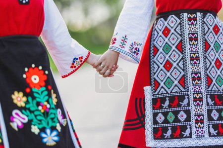 Téléchargez les photos : Filles en costumes ethniques bulgares traditionnels avec broderie folklorique tenant la main. L'esprit de la Bulgarie - culture, histoire et traditions. - en image libre de droit