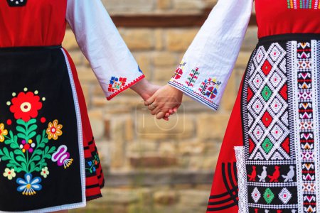 Foto de Chicas con trajes étnicos bulgaros tradicionales con bordados folclóricos tomados de la mano. El espíritu de Bulgaria - cultura, historia y tradiciones. - Imagen libre de derechos