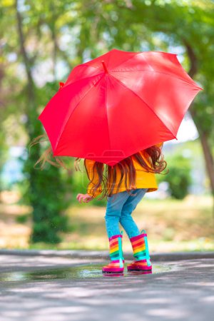 Photo for Happy beautiful girl with umbrella and color rubber boots jump on a rainy puddle - Royalty Free Image