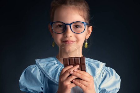 Téléchargez les photos : Chocolat et jolie petite femme affamée portrait. Belle fille intelligente avec des lunettes prêtes à manger barre de chocolat. - en image libre de droit