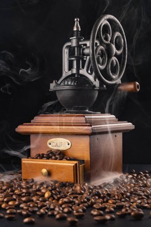 Téléchargez les photos : Mélangeur de moulin à café vintage avec grains de café et fumée d'arôme isolé sur fond noir - en image libre de droit