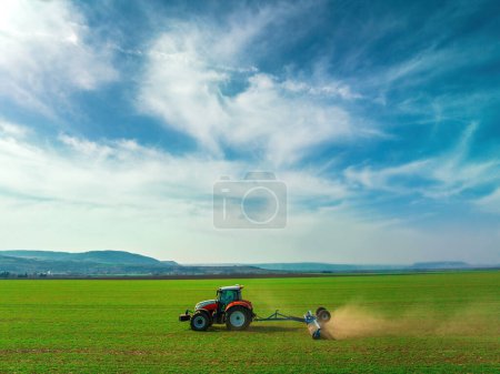Foto de Tractor con una labranza de rodillos en el campo de primavera. Vista aérea del suelo El balanceo apoya la germinación y es la base para una buena cosecha, agricultura orgánica y agronomía - Imagen libre de derechos