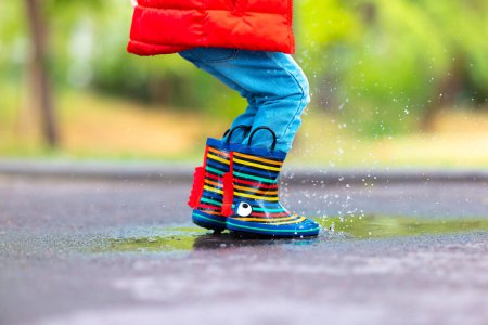 Foto de Pies de niño con coloridas botas de goma saltando sobre un charco lluvioso en un parque - Imagen libre de derechos