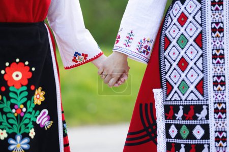 Foto de Chicas con trajes étnicos bulgaros tradicionales con bordados folclóricos tomados de la mano. El espíritu de Bulgaria - cultura, historia y tradiciones. - Imagen libre de derechos