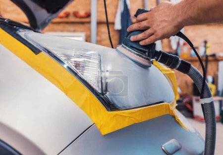 Photo for Car polishing service - car cleaner specialist polishing headlamp with polish machine in workshop garage - Royalty Free Image