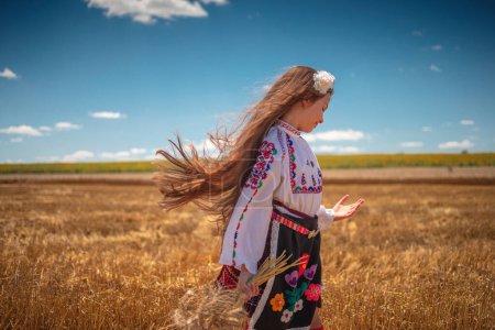 Photo for Girl in traditional ethnic folklore costume with Bulgarian embroidery standing on a harvest golden wheat field - Royalty Free Image