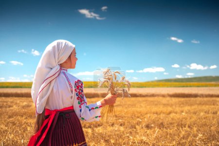 Téléchargez les photos : Fille en costume folklorique ethnique traditionnel avec broderie bulgare debout sur un champ de blé doré moisson - en image libre de droit