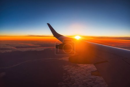 Photo for Airplane flight in sunset sky over ocean water and wing of plane. View from the window of the Aircraft. Traveling in air. - Royalty Free Image