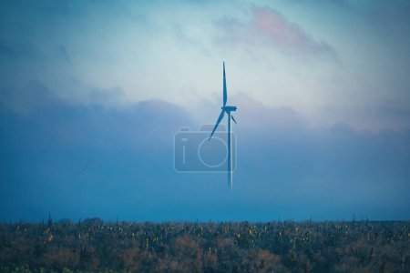 Téléchargez les photos : Hélice éolienne électrique travaillant sur le lever du soleil brumeux sur un champ agricole à la campagne - en image libre de droit