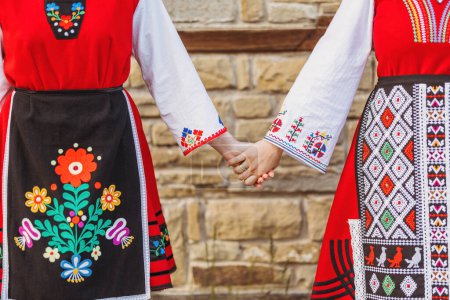 Téléchargez les photos : Filles en costumes ethniques bulgares traditionnels avec broderie folklorique tenant la main. L'esprit de la Bulgarie - culture, histoire et traditions. - en image libre de droit