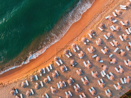 Téléchargez les photos : Vue aérienne du dessus depuis un drone de plage de sable avec des vagues de mer turquoise, des parasols et des chaises longues avec espace de copie pour le texte - en image libre de droit