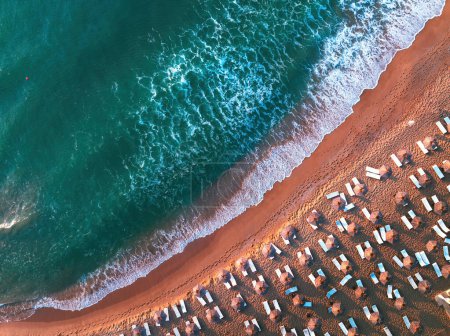 Téléchargez les photos : Vue aérienne sur la plage. Parapluies, vagues de sable et de merVue aérienne depuis le drone de la plage de sable avec vagues de mer turquoise, parasols et chaises longues avec espace de copie pour le texte - en image libre de droit