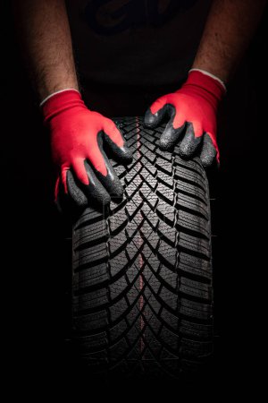 Foto de Servicio de neumáticos de coche y manos de mecánico sosteniendo neumático nuevo sobre fondo negro con espacio de copia para texto - Imagen libre de derechos