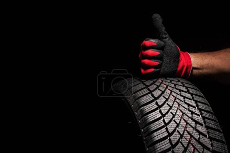 Téléchargez les photos : Service de pneus de voiture et les mains du mécanicien tenant un pneu neuf sur fond noir avec espace de copie pour le texte - en image libre de droit