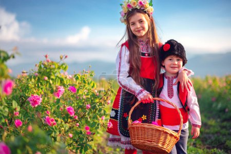 Bulgarisches Rosenfeld Damascena, Rosental Kazanlak, Bulgarien. Junge und Mädchen in ethnischer Folklorekleidung ernten bei Sonnenaufgang ölhaltige Rosen.