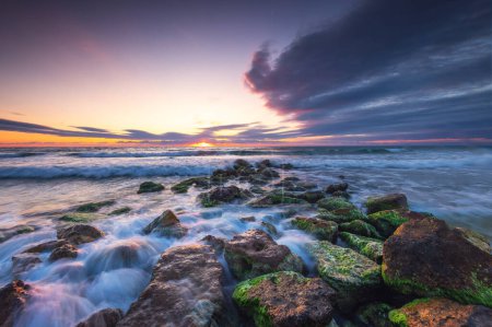 Foto de Salida del sol paisaje nuboso sobre las olas del mar y la playa rocosa orilla, costa salvaje y horizonte oceánico - Imagen libre de derechos