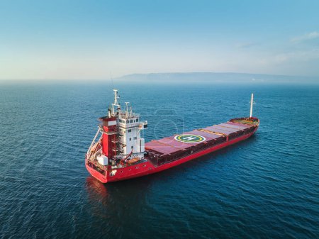 Téléchargez les photos : Lever de soleil sur l'horizon océanique et voilier industriel cargo en eaux libres bleu profond, vue aérienne - en image libre de droit