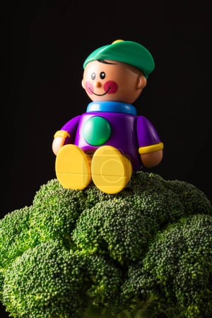 Foto de Flores de brócoli fresco y juguete de plástico niño sobre fondo rústico negro - Imagen libre de derechos