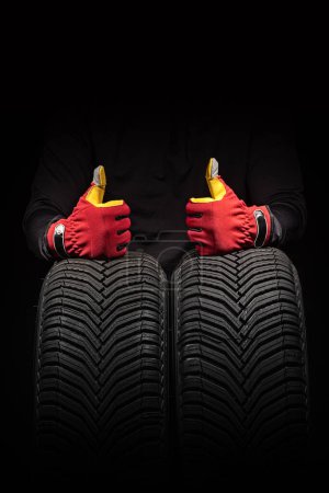 Foto de Servicio de neumáticos de coche y manos de mecánico sosteniendo neumático nuevo sobre fondo negro con espacio de copia para texto, vertical - Imagen libre de derechos