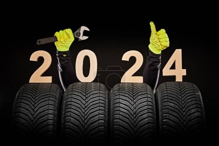 Téléchargez les photos : Service de pneus de voiture d'hiver et pouces levés mains de mécanicien et de texte 2024 bonne année sur fond noir - en image libre de droit