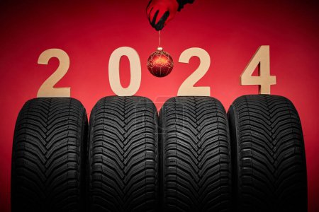 Photo for Winter car tires and man hand in red gloves hold christmas tree ball, 2024 happy new year background. - Royalty Free Image