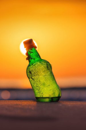 Téléchargez les photos : Bouteille sur la plage sable et eau pendant le lever du soleil doré sur l'horizon de la mer - en image libre de droit