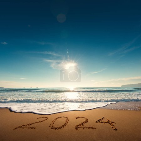 Foto de Hermoso paisaje nublado sobre el mar, toma el sol. Feliz Año Nuevo 2024 escrito en la orilla del mar. - Imagen libre de derechos