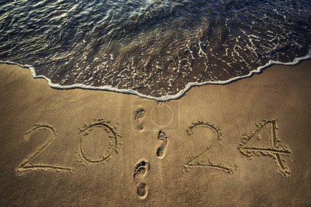 Photo for Happy New Year 2024 concept on the sea sand at sunrise and footprints on the beach - Royalty Free Image