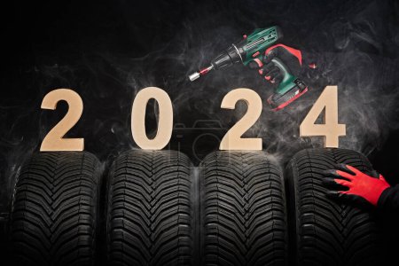 Photo for 2024 happy new year, winter care tires and hands of a man with screwdriver for wheels on black background. - Royalty Free Image