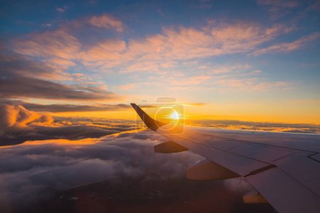 Téléchargez les photos : Vol en avion au coucher du soleil au-dessus de l'eau de l'océan et de l'aile de l'avion. Vue de la fenêtre de l'avion. Voyager dans l'air. - en image libre de droit