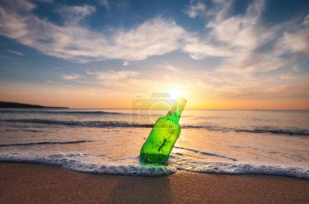 Téléchargez les photos : Lever de soleil sur la mer et bouteille de bière sur la plage sable et éclaboussures vagues sur le coup - en image libre de droit