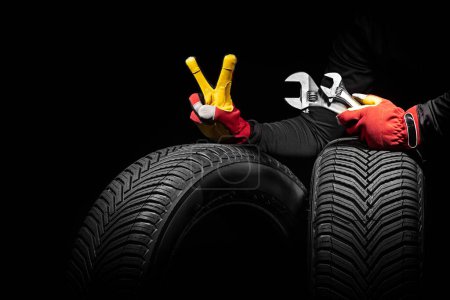 Foto de Servicio de neumáticos de coche de invierno y manos de mecánico con llave inglesa, destornillador sobre fondo negro - Imagen libre de derechos