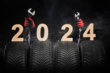 Téléchargez les photos : Pneus de voiture, roues d'hiver, pneus neufs dans le brouillard et les mains du mécanicien avec des instruments de clé, heureux nouvel an 2024 fond noir . - en image libre de droit