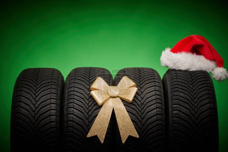 Foto de Neumáticos de coche, neumáticos nuevos, ruedas de invierno aisladas sobre fondo de navidad verde con cinta de lazo presente y sombrero de Santa Claus - Imagen libre de derechos