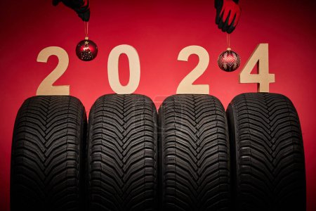 Foto de Neumáticos de invierno, servicio de ruedas grandes y manos de la mecánica con bola de árbol de Navidad en el nuevo año 2024 fondo rojo. - Imagen libre de derechos