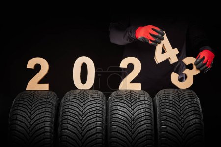 Téléchargez les photos : Voiture pneus service et les mains de numéro de mécanicien texte 2023 2024 année sur fond noir - en image libre de droit