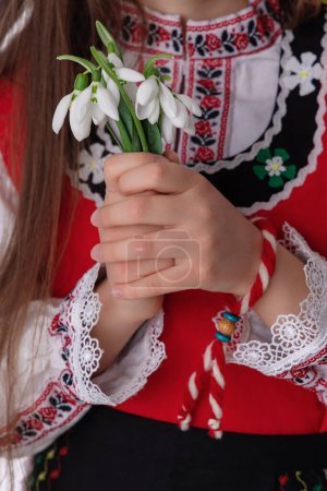 Foto de Mujer búlgara en traje de bordado folclore étnico nosia, martenitsa pulsera de hilo, y el ramo de primavera gotas de nieve símbolo de la cultura y el espíritu de Bulgaria - Imagen libre de derechos