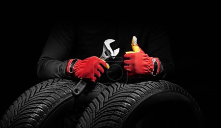 Foto de Servicio de neumáticos de coche de invierno y manos de mecánico con llave inglesa, destornillador sobre fondo negro - Imagen libre de derechos