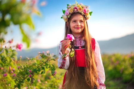 Foto de Hermosa chica búlgara en vestido folclore étnico tradicional y rosas aromáticas de aceite en el campo en flor, Kazanlak, Bulgaria - Imagen libre de derechos