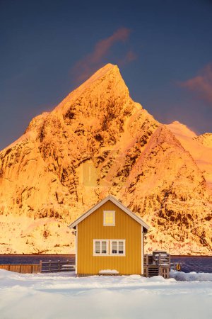 Foto de Islas Lofoten hermoso paisaje de la puesta del sol naturaleza en Noruega y la ciudad de pesca con pintoresca casa rorbu amarillo de Sakrisoy, Reine - Imagen libre de derechos