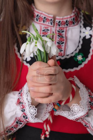Foto de Chica búlgara con flores de primavera nevadas y artesanía pulsera de lana martenitsa símbolo de Baba Marta, marzo, Bulgaria - Imagen libre de derechos