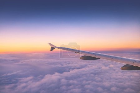 Foto de Avión volando sobre nubes de cielo de color durante el atardecer escénico o el amanecer paisaje nublado, vista desde la ventana plana de las turbinas de alas y el horizonte - Imagen libre de derechos