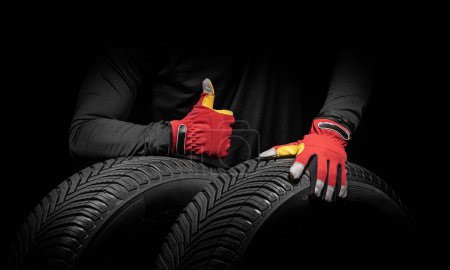 Foto de Servicio de neumáticos de coche y manos de mecánico sosteniendo neumático nuevo sobre fondo negro con espacio de copia para texto. - Imagen libre de derechos