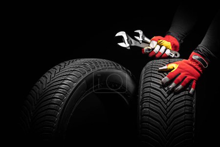 Foto de Servicio de neumáticos de coche y manos de mecánico sosteniendo neumático nuevo y llave inglesa sobre fondo negro con espacio de copia para texto - Imagen libre de derechos